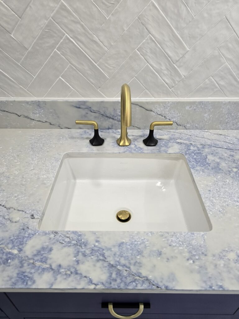 Detail of a custom bathroom sink featuring gold fixtures and natural stone countertop.