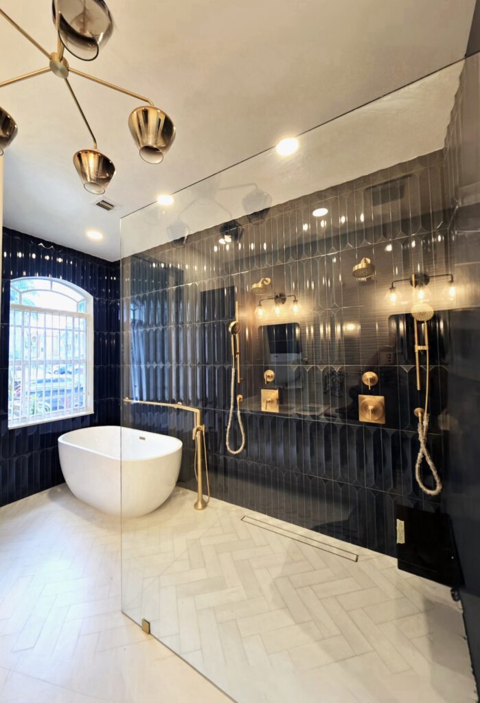Bespoke ADA-compliant luxury bathroom featuring a barrier-free wet room layout, deep soaking tub, dark blue vertical tile work, and elegant brass fixtures
