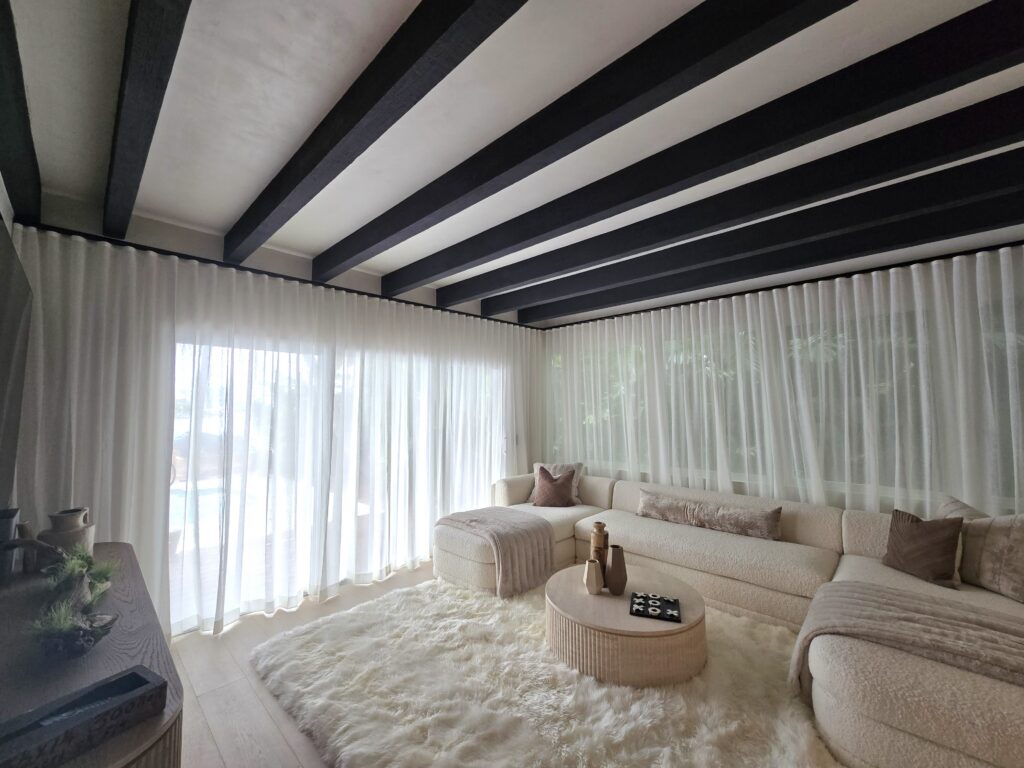 Bespoke living room interior with dark ceiling beams and floor-to-ceiling sheer drapes